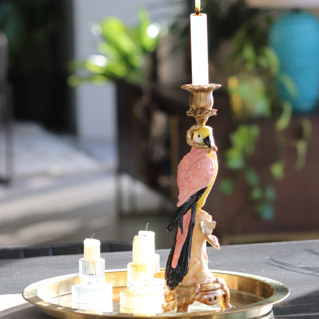 Antiqued gold parrot candle holder sits on a gold tray with some small glass candle holders beside it