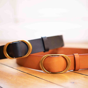 two Classic soft leather belts with a brass buckle sit on top of each other, one black belt, one brown belt