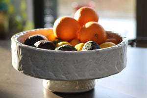 white textured bowl made from terracotta with fruit in it, sits on table