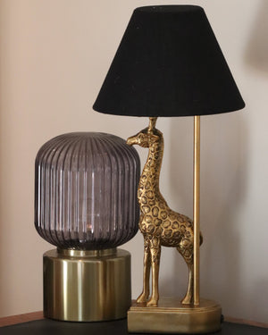 gold coloured giraffe table lamp with black shade sits next to a gold based lamp with glass dome top