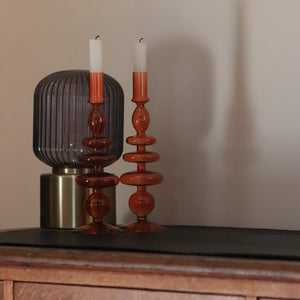 Two Orange bobble glass candlestick holders sat  on a wooden table with gold light in background 