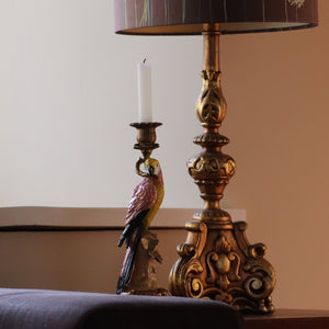 Wooden Parrot Colourful Candlestick Holder next to an ornate gold lamp stand by a window