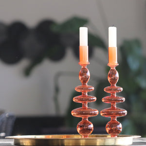 Two Orange bobble glass candlestick holders sat in a gold tray with artwork in background