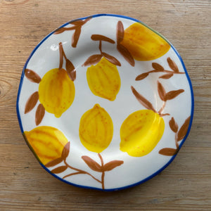 A stoneware plate with brown twigs and lemons sits on a brown table