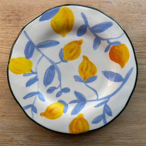 A stoneware plate with light blue twigs and lemons sits on a brown table