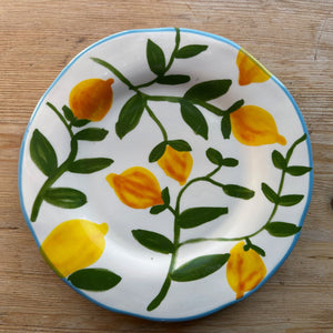 A stoneware plate with green twigs and lemons sits on a brown table