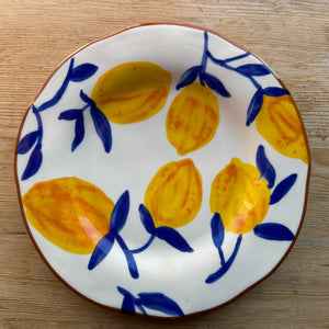 A stoneware plate with navy twigs and lemons sits on a brown table