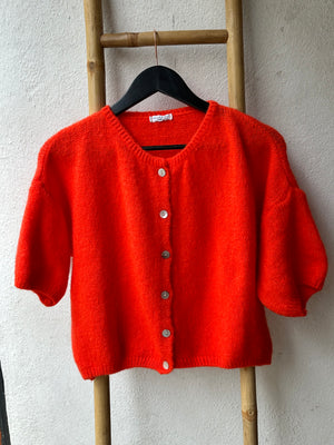 a mohair mix poppy red cardigan with three quarter length sleeves is hung on a wooden ladder against a white wall