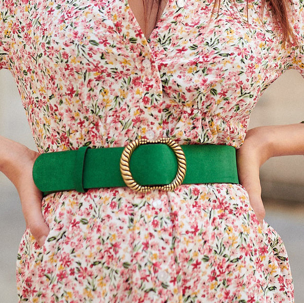 a model wears a green suede  wide belt with a  large brass buckle over a floral dress