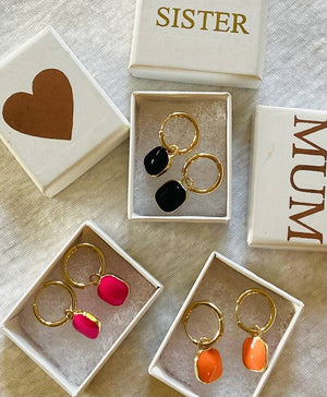 3 sets of colour pop earrings sitting in open gift boxes.  Gold hoops with enamel square colour pops in pink, orange and black with gift box with heart, sister and mum written in gold on the lid