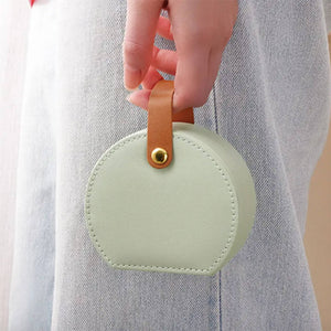 a woman's hand holds a  sage green jewellery case by its brown leather handle