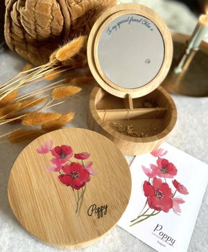 Round wooden personalised jewellery box in forefront with poppy flower picture and the word poppy engraved onto it.  In the background  the box is open showing a mirror and a card with the details of the birth flower