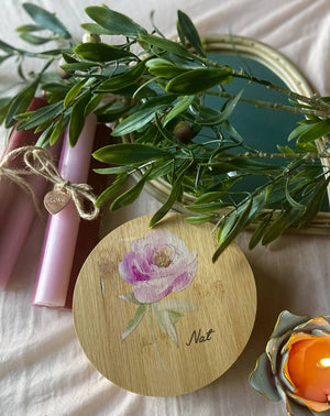 Round wooden personalised jewellery box in forefront with rose flower picture and the word Nat engraved onto it.  Beside the box is a pink candle wrapped in a string bow with a heart engraved with love attached