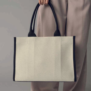 woman hold tote bag with black handle and edges and cream/natural body