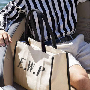 Man in shorts and a striped shirt sits next to contrast black and white tote with initials EWP embroidered on the tote