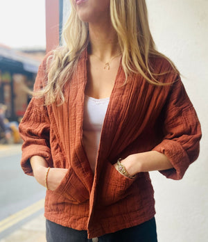 Model wears a rust coloured quilted jacket with rolled up sleeves