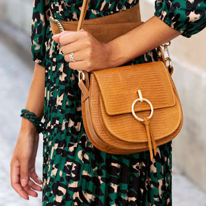 Model carries a compact tan cross body saddle bag with a brass buckle ring